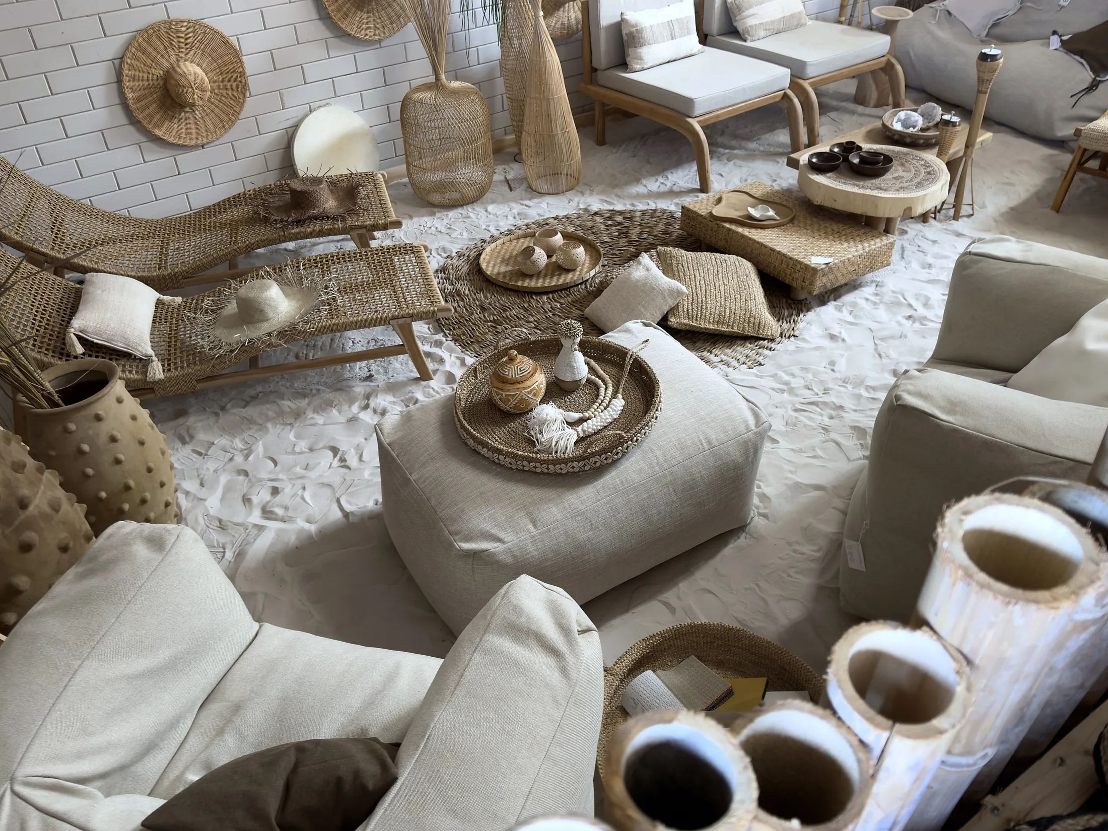 Loungehoek van The Outdoor Lab bij CoCo homeliving met kussens en poefs op een zandvloer, en strohoeden aan een witte muur