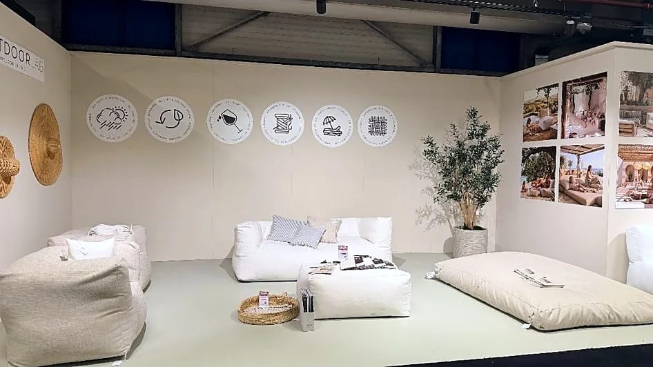 Vooraanzicht van onze stand bij TICA Projects Venlo met loungebank, poefs en liggend kussen tegen een wand met merkiconen en moodboards