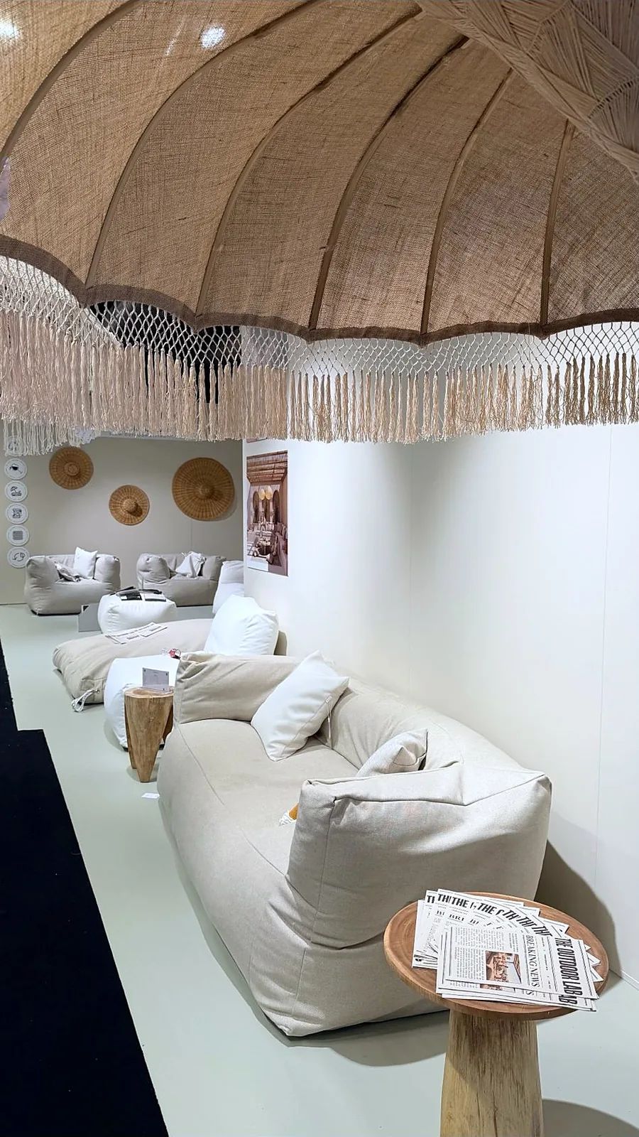 Loungebank in linnen stof onder een macramé parasol met franjes bij TICA Projects Venlo, met exemplaren van The Outdoor Lab-krant op een houten bijzettafeltje