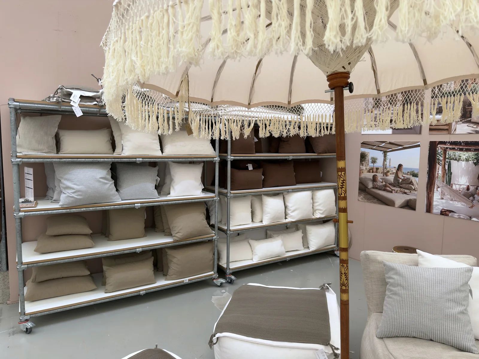 Rek met opgevouwen outdoor kussens in verschillende stoffen en kleuren, met sfeerbeelden aan de wand erachter