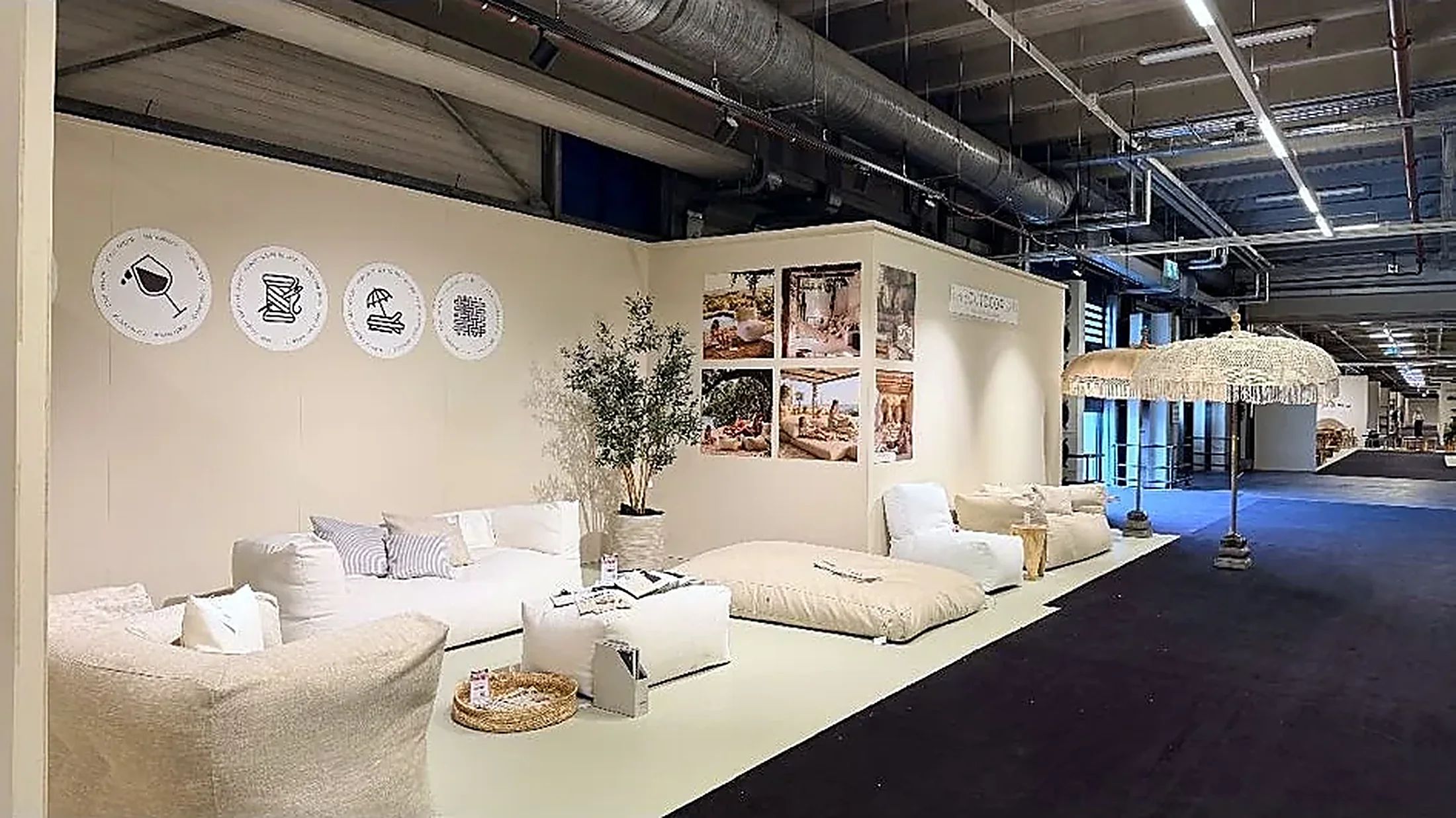 Onze stand bij TICA Projects Venlo met loungebank, poefs en een liggend kussen rond een kunstolijfboom, met een macramé parasol ernaast en moodboards aan de wand