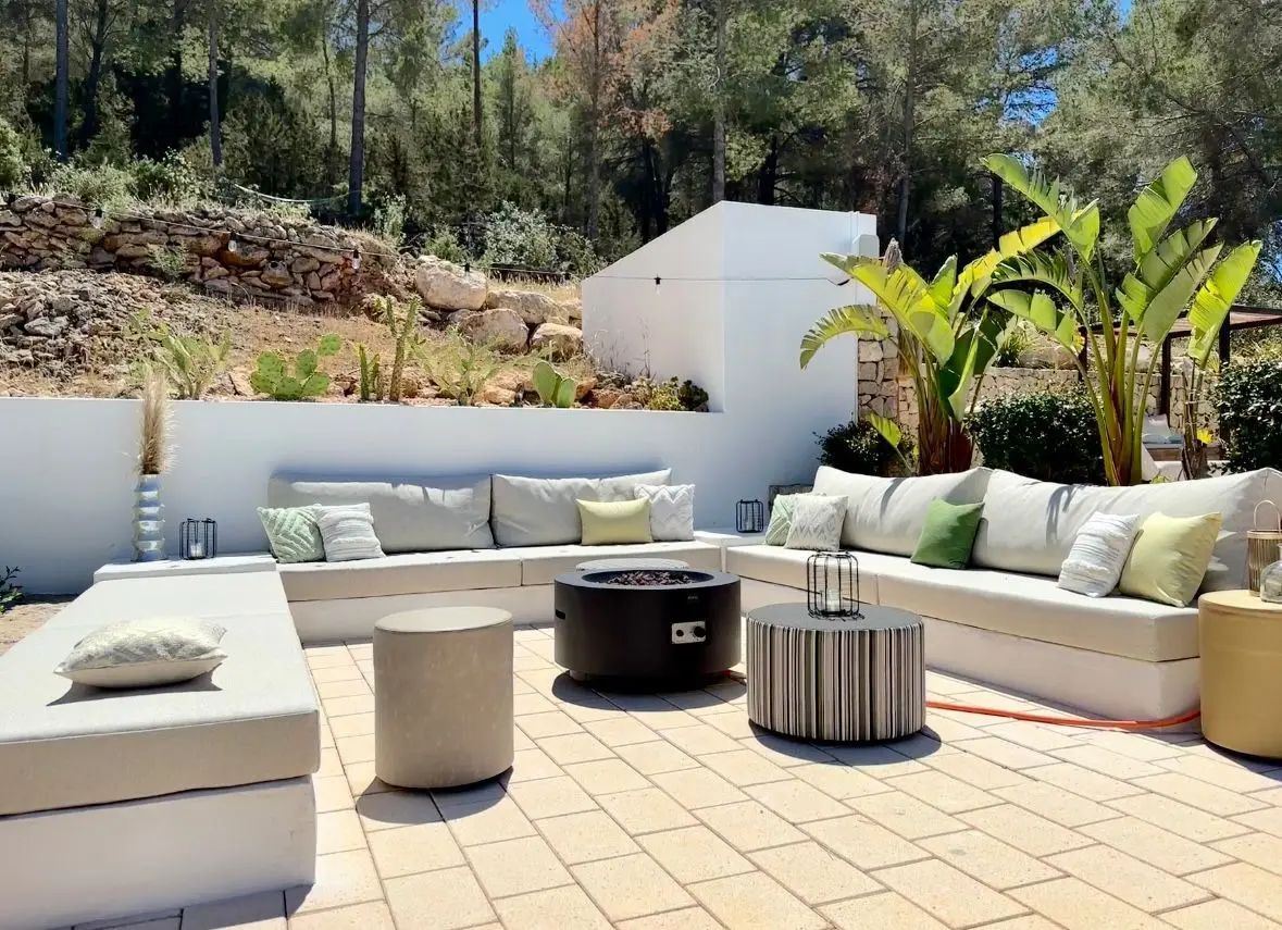 Mediterraan terras met een L-vormige loungebank vol buitenkussens rond een vuurtafel